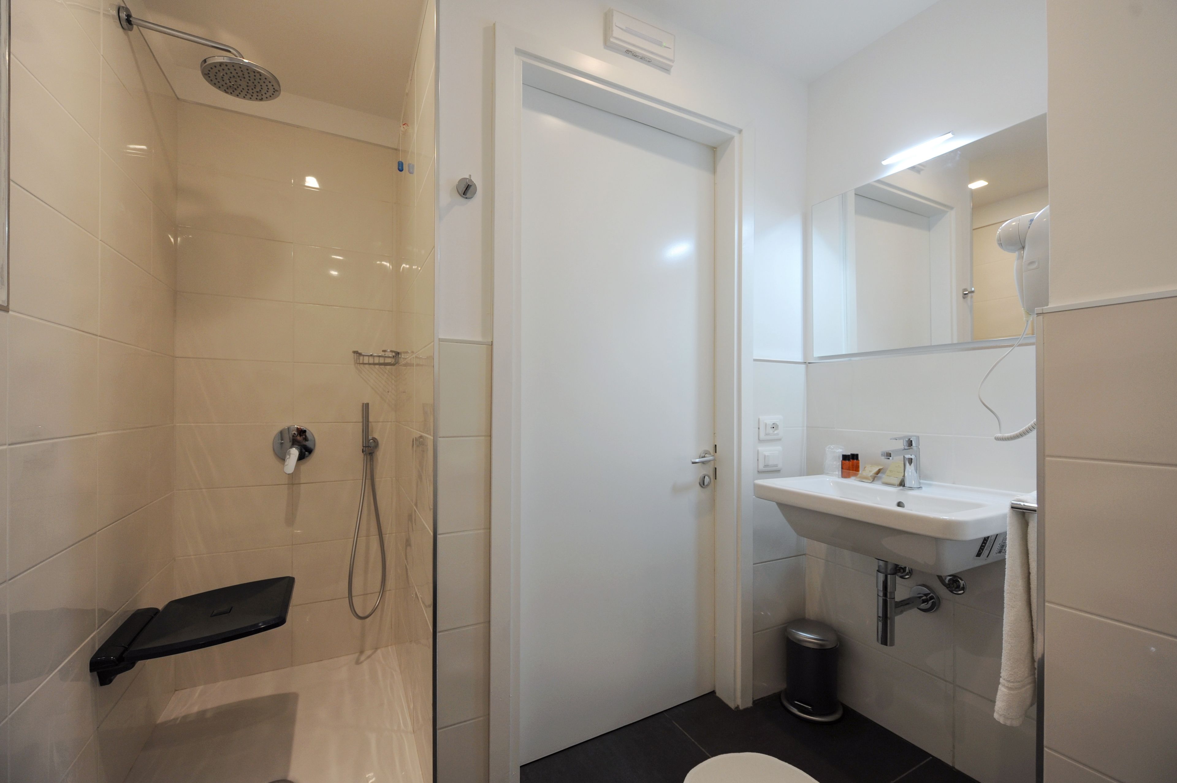 Uma casa de banho moderna com chuveiro em cabine de vidro, lavatório branco e espelho sobre o lavatório.