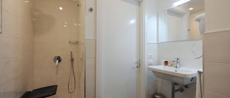 Uma casa de banho moderna com chuveiro em cabine de vidro, lavatório branco e espelho sobre o lavatório.