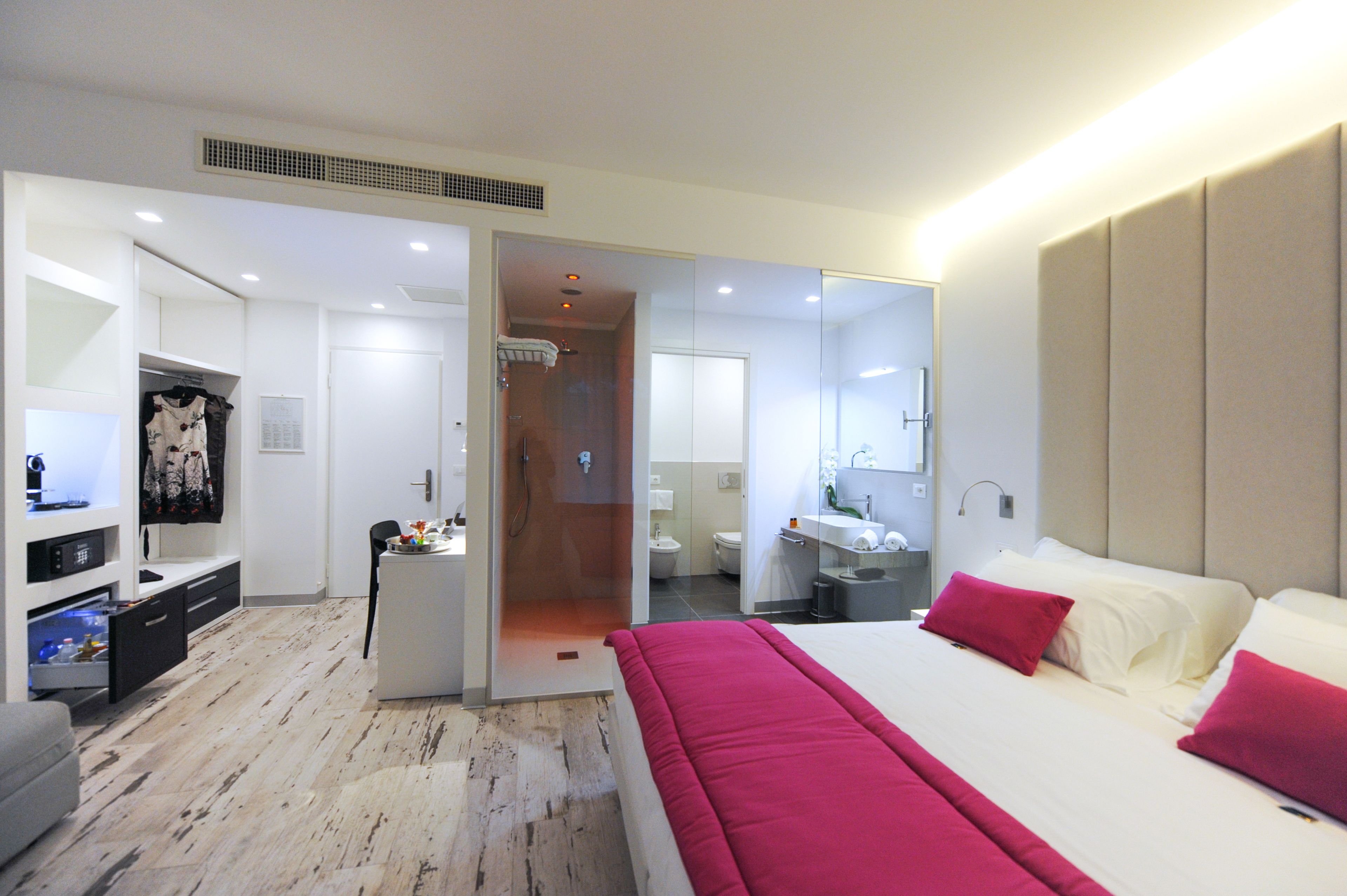 A modern hotel room with a large bed, a walk-in closet, a bathroom with a shower, and a desk with a chair.