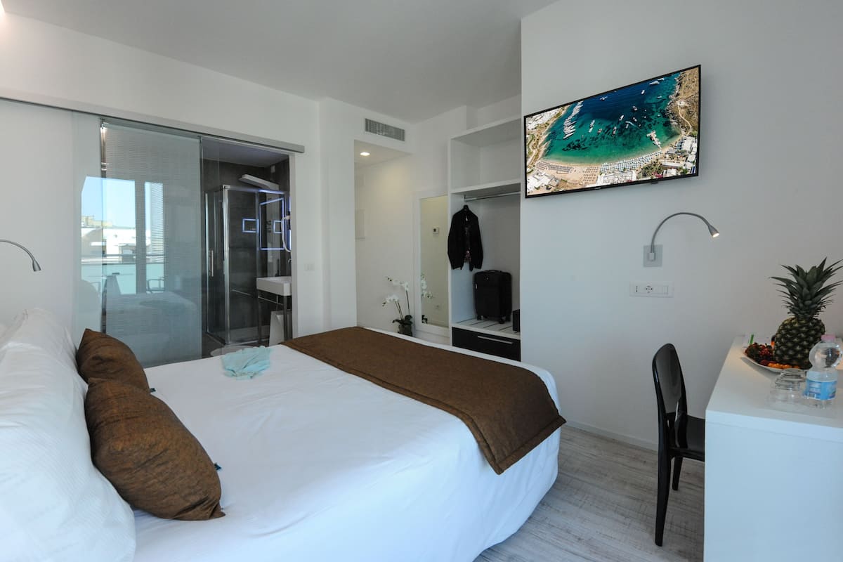 Een moderne hotelkamer met een bed, een bureau, een stoel, een televisie en uitzicht op zee.