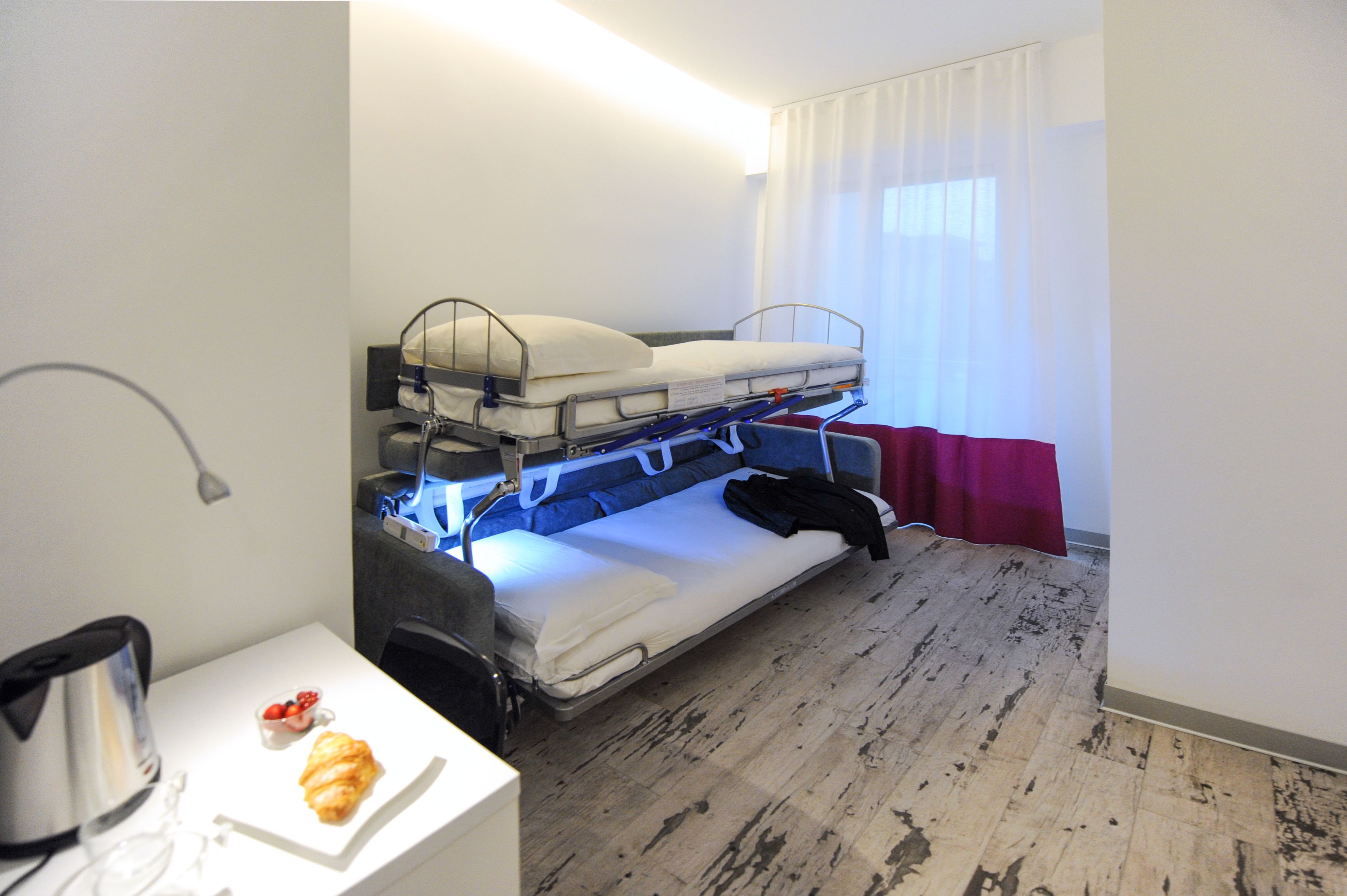 A bunk bed room with a small table, a kettle, and a pastry.