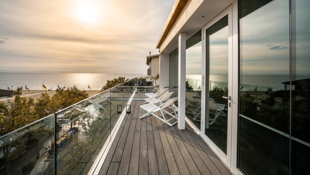 A balcony with a view of the sea, white lounge chairs, and a glass railing. - Hotel Lampara (Lignano Sabbiadoro)