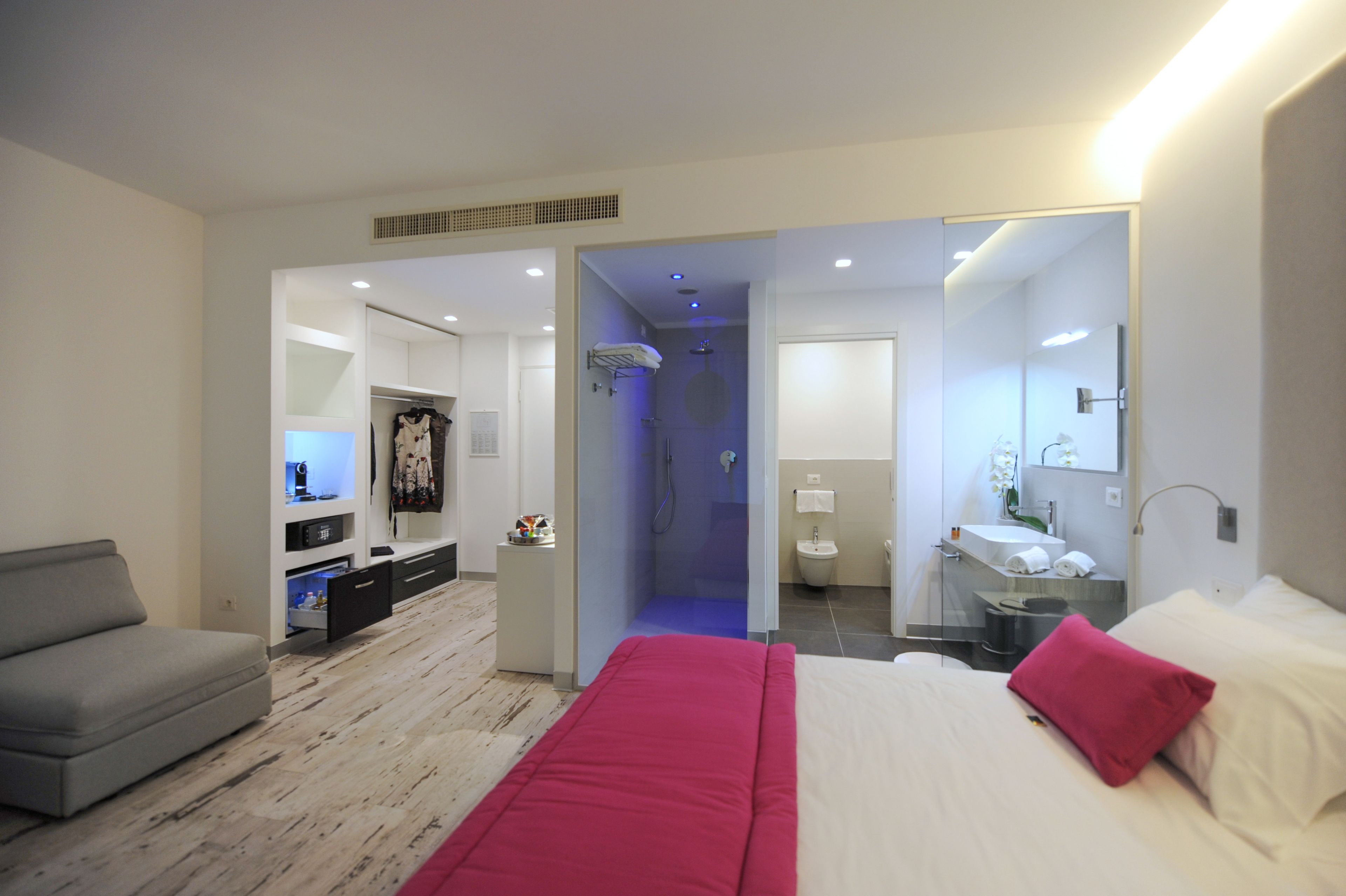 Et moderne hotelværelse med seng, grå sofa, walk-in garderobe, badeværelse med bruser og et lille skrivebord.