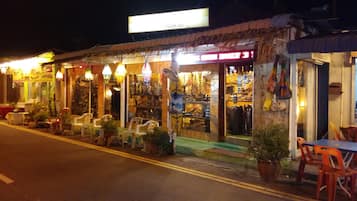 A street-side shop with a signboard, outdoor seating, and various items displayed outside.