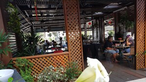 An outdoor seating area with tables and chairs, surrounded by potted plants and a wooden lattice structure. - D'Feringghi Haus Hotel & Restaurant (George Town)