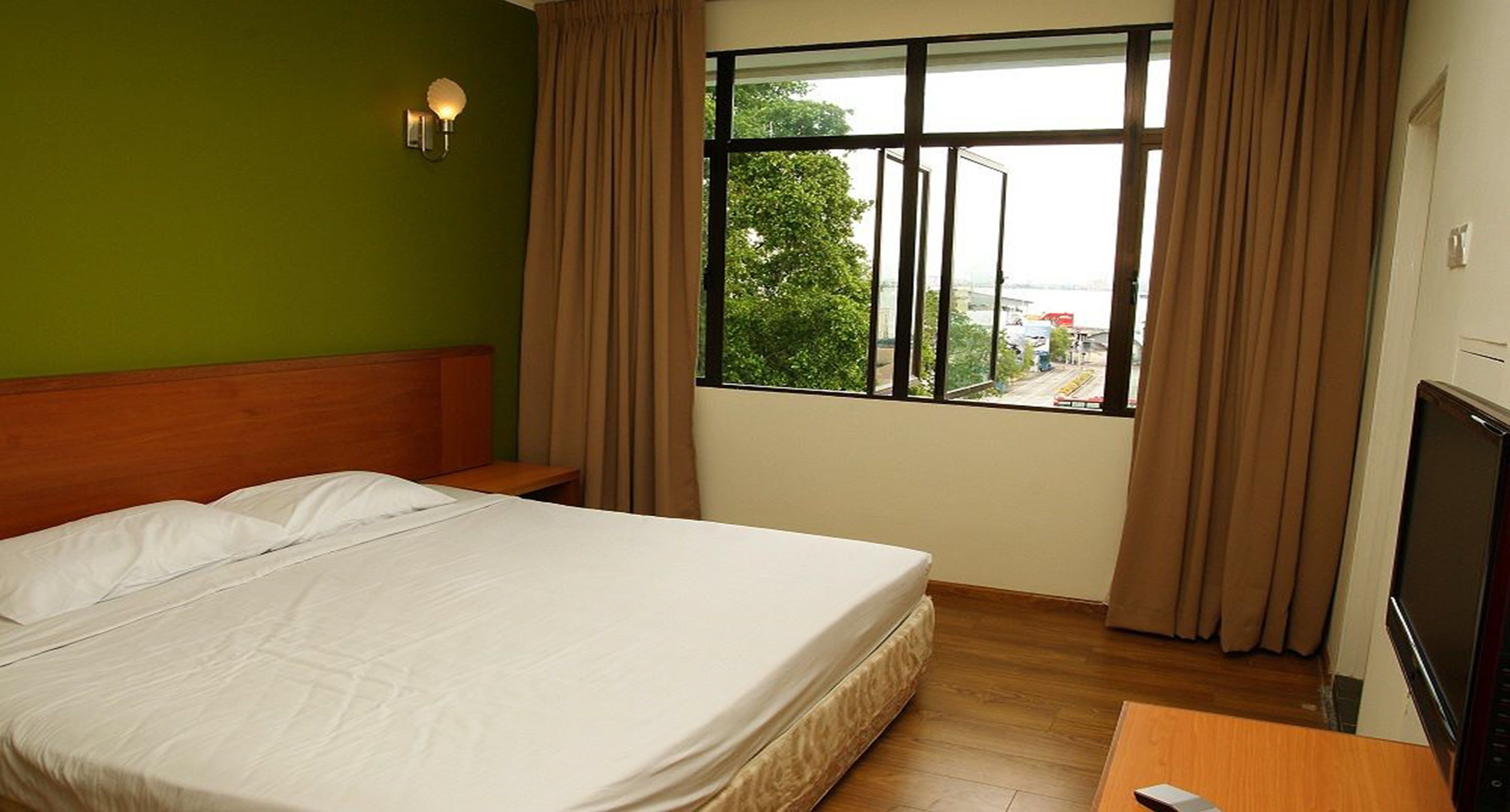 A hotel room with a bed, a TV, a window with curtains, and a view of the outside.