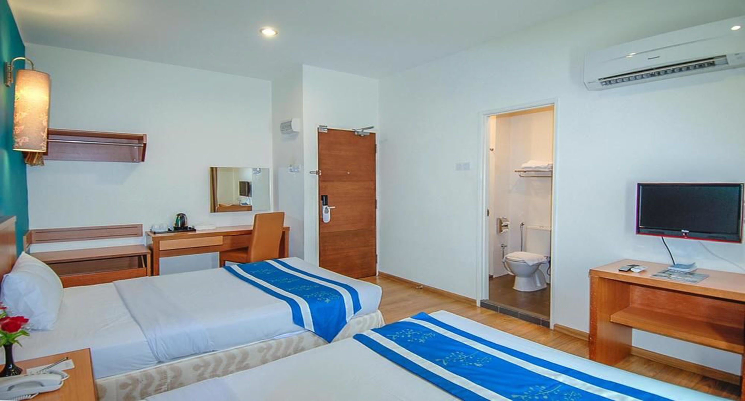 Habitación de hotel con dos camas, un escritorio con silla, televisión y baño visible a través de una puerta abierta.