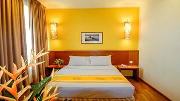 Una habitación de hotel con cama, mesita de noche, lámpara, un cuadro en la pared y una planta.