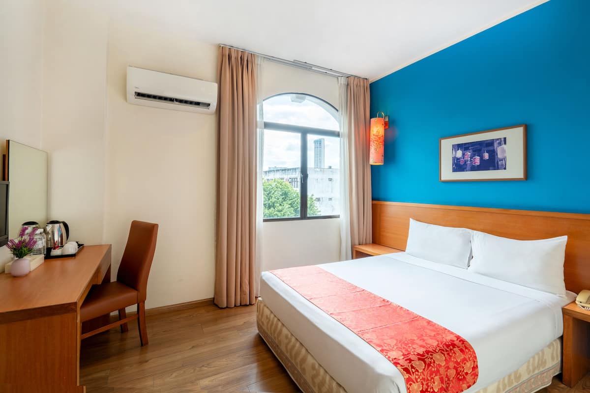Una camera d'albergo con un letto, una scrivania con sedia, un condizionatore d'aria, una finestra con tende, un quadro appeso al muro e un comodino con telefono.