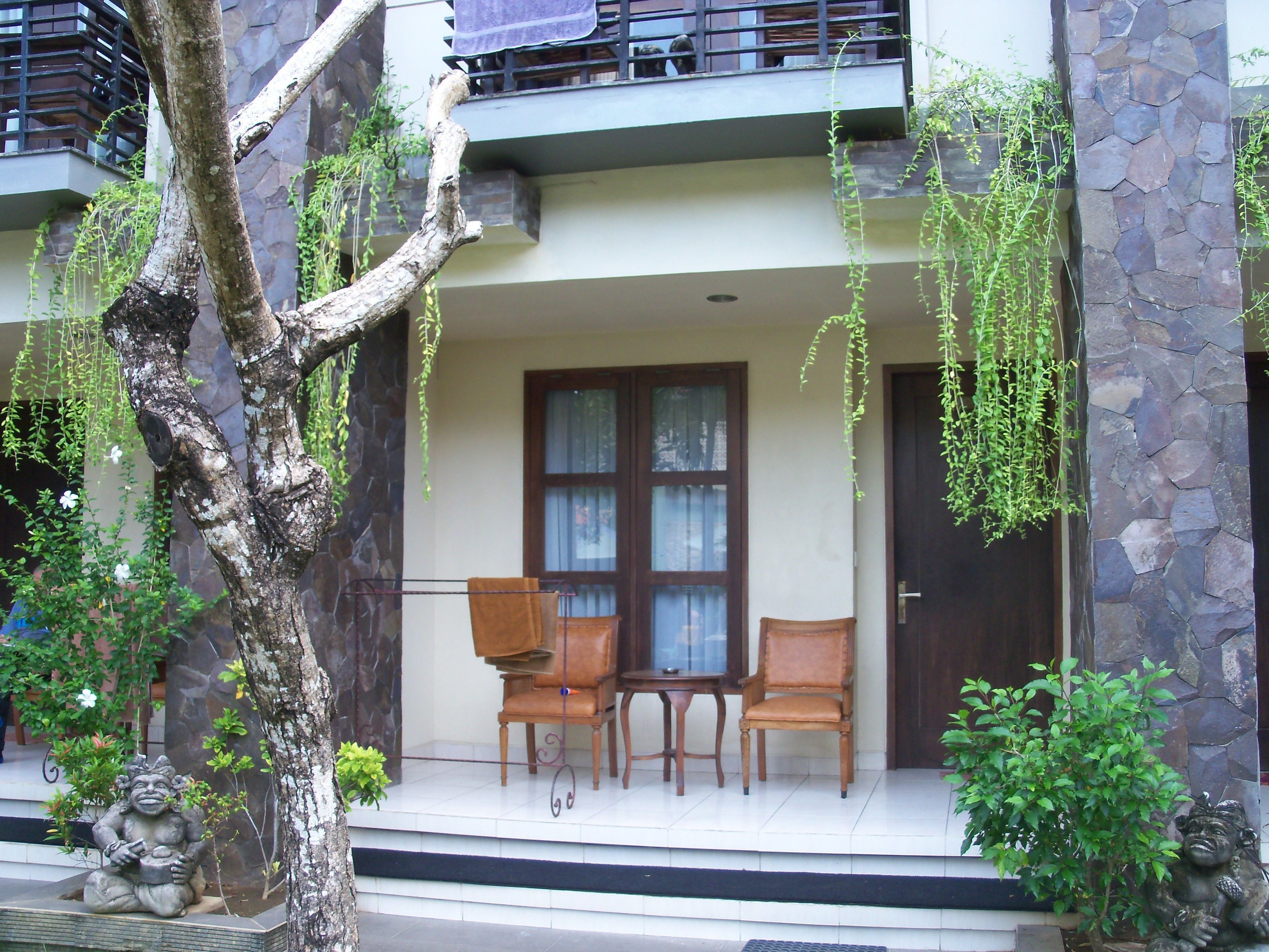 A building with a stone facade, a balcony with a metal railing, and a seating area with two chairs and a table.