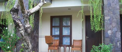 A building with a stone facade, a balcony with a metal railing, and a seating area with two chairs and a table.