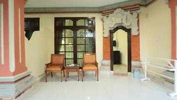 A room with two wooden chairs, a small table, and a large window with curtains.