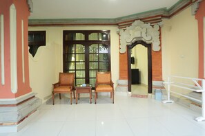 A room with two wooden chairs, a small table, and a large window with curtains. - La Walon Hotel (Kuta)