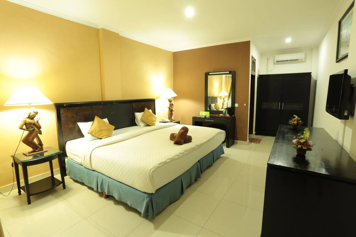 Habitación de hotel con una cama grande, dos mesitas de noche con lámparas, un aparador, un espejo y un televisor en la pared.
