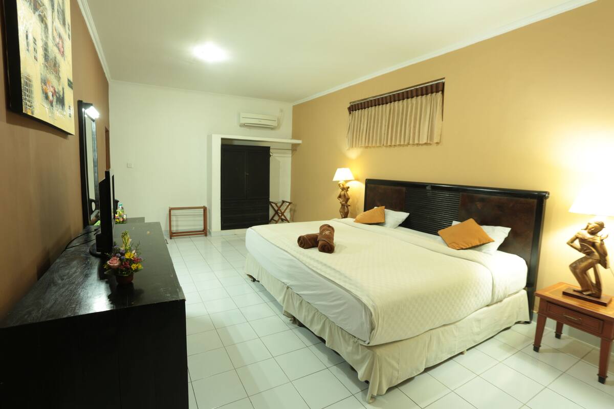 Habitación de hotel con una cama grande, un escritorio con lámpara y una pequeña estatua en la mesita de noche.