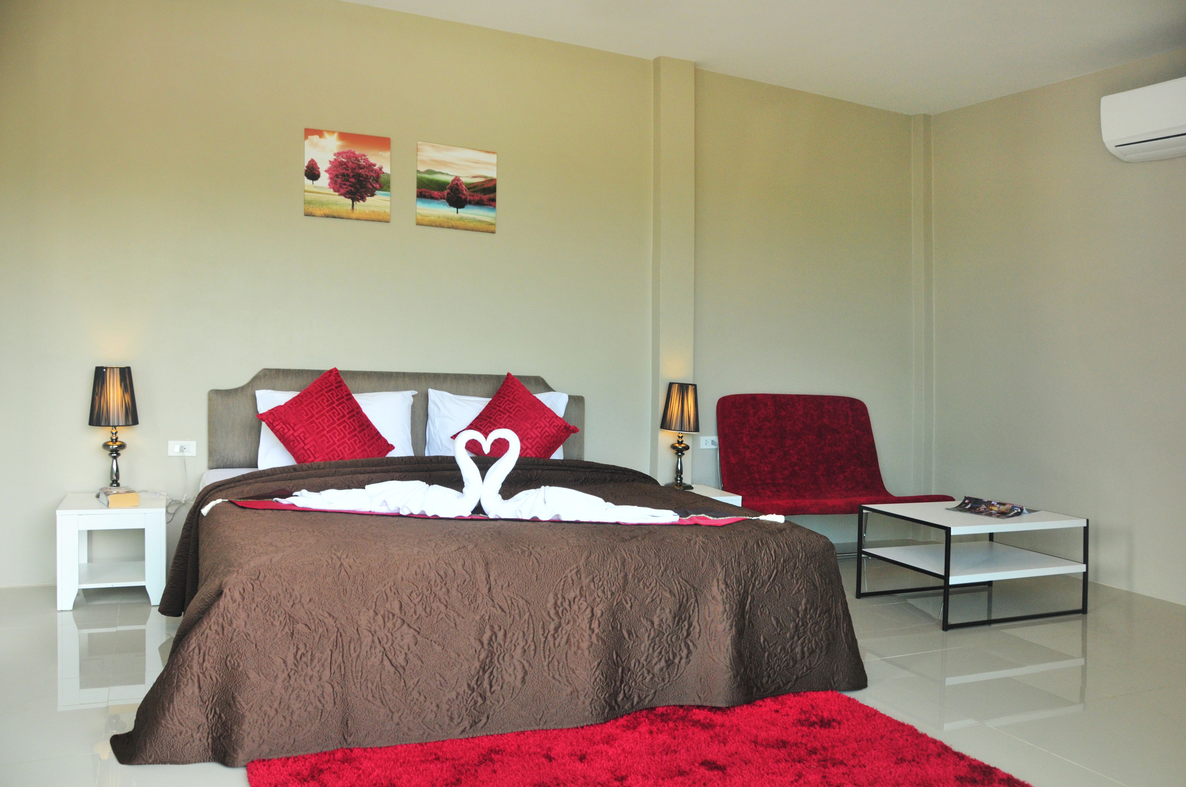 Une chambre d’hôtel moderne avec un grand lit, deux tables de chevet, un fauteuil rouge et une petite table sur laquelle repose un magazine.