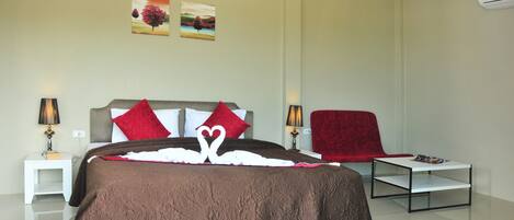 Une chambre d’hôtel moderne avec un grand lit, deux tables de chevet, un fauteuil rouge et une petite table sur laquelle repose un magazine.
