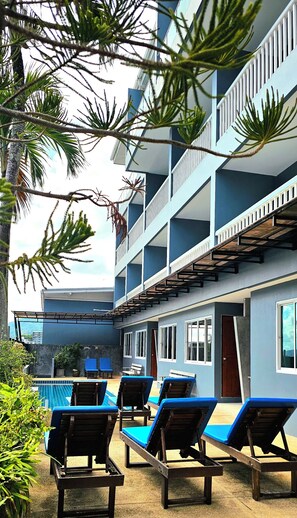A multi-story building with balconies, a pool area with sun loungers, and surrounding greenery. - Am Surin Place (Choeng Thale)