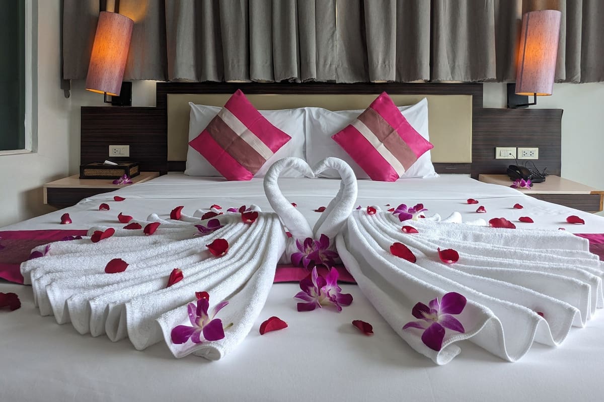 Quarto de hotel com cama bem arrumada, duas luminárias de cabeceira e uma janela grande com cortinas.