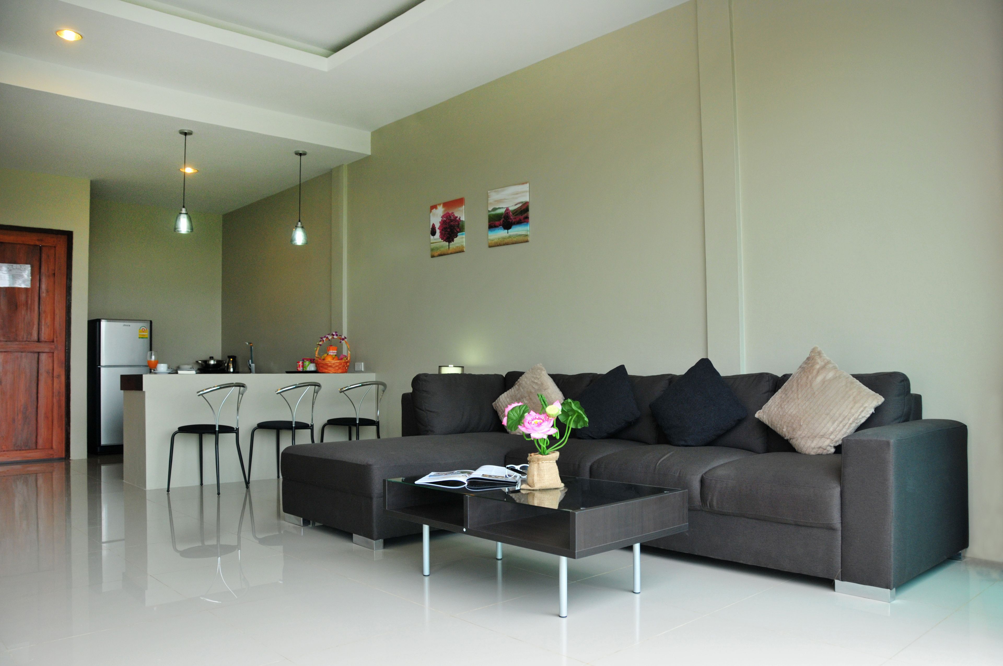 Een moderne woonkamer met een grijze bank, zwarte stoelen, een glazen salontafel en een keuken in de achtergrond.