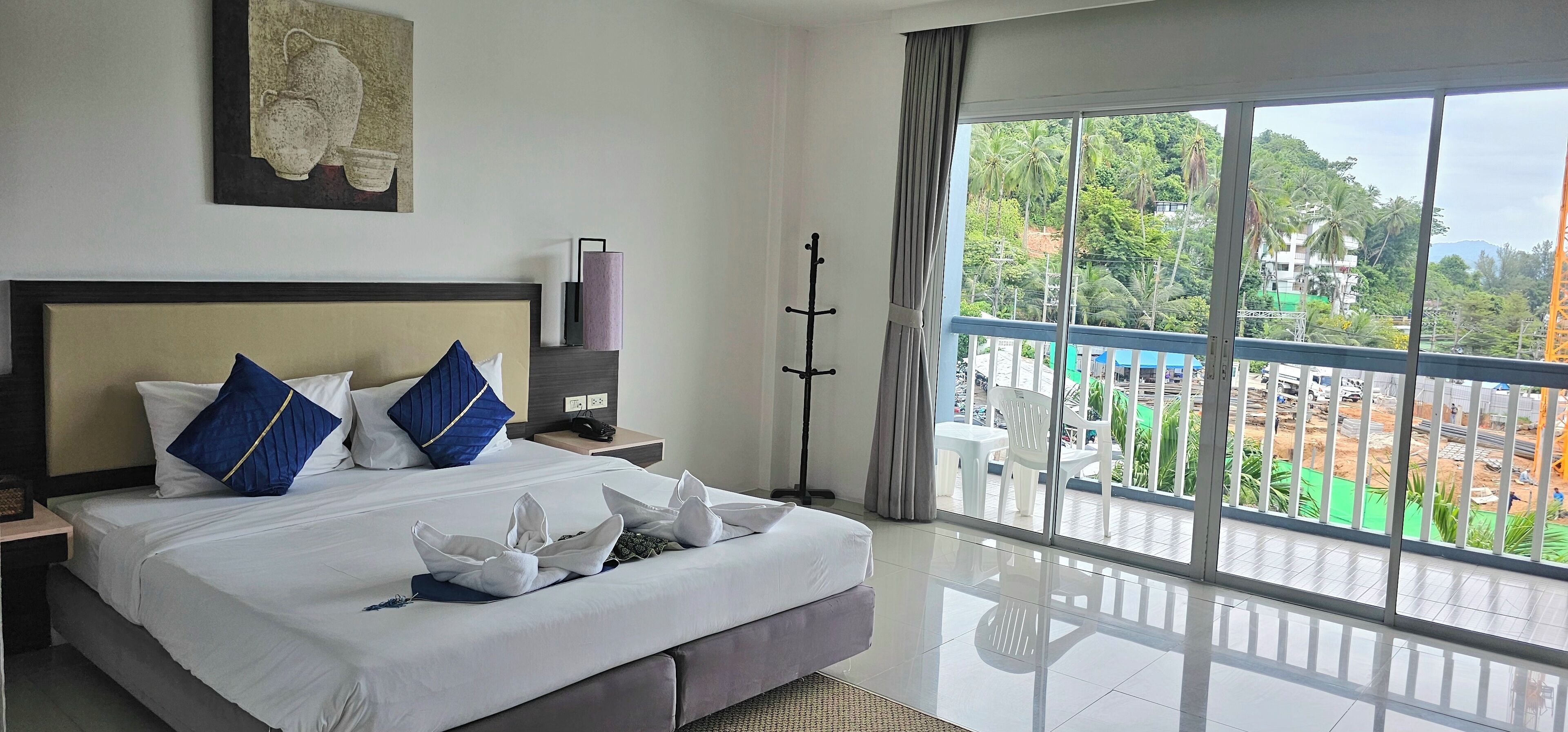 A hotel room with a large bed, a nightstand, a lamp, and a view of the outside.
