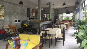 Ein großzügiges Café mit hohen Decken, mehreren Deckenventilatoren und verschiedenen Sitzgelegenheiten, darunter Tische und Stühle.