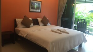 Ein Hotelzimmer mit einem Bett, Kissen, einem Nachttisch, einem gerahmten Bild an der Wand und Blick ins Grüne durch das Fenster.