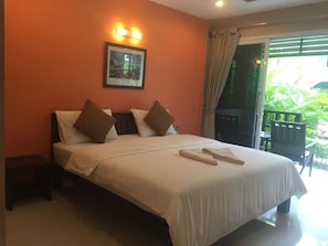 Quarto de hotel com cama, almofadas, mesa de cabeceira, uma fotografia emoldurada na parede e vista para o verde pela janela.