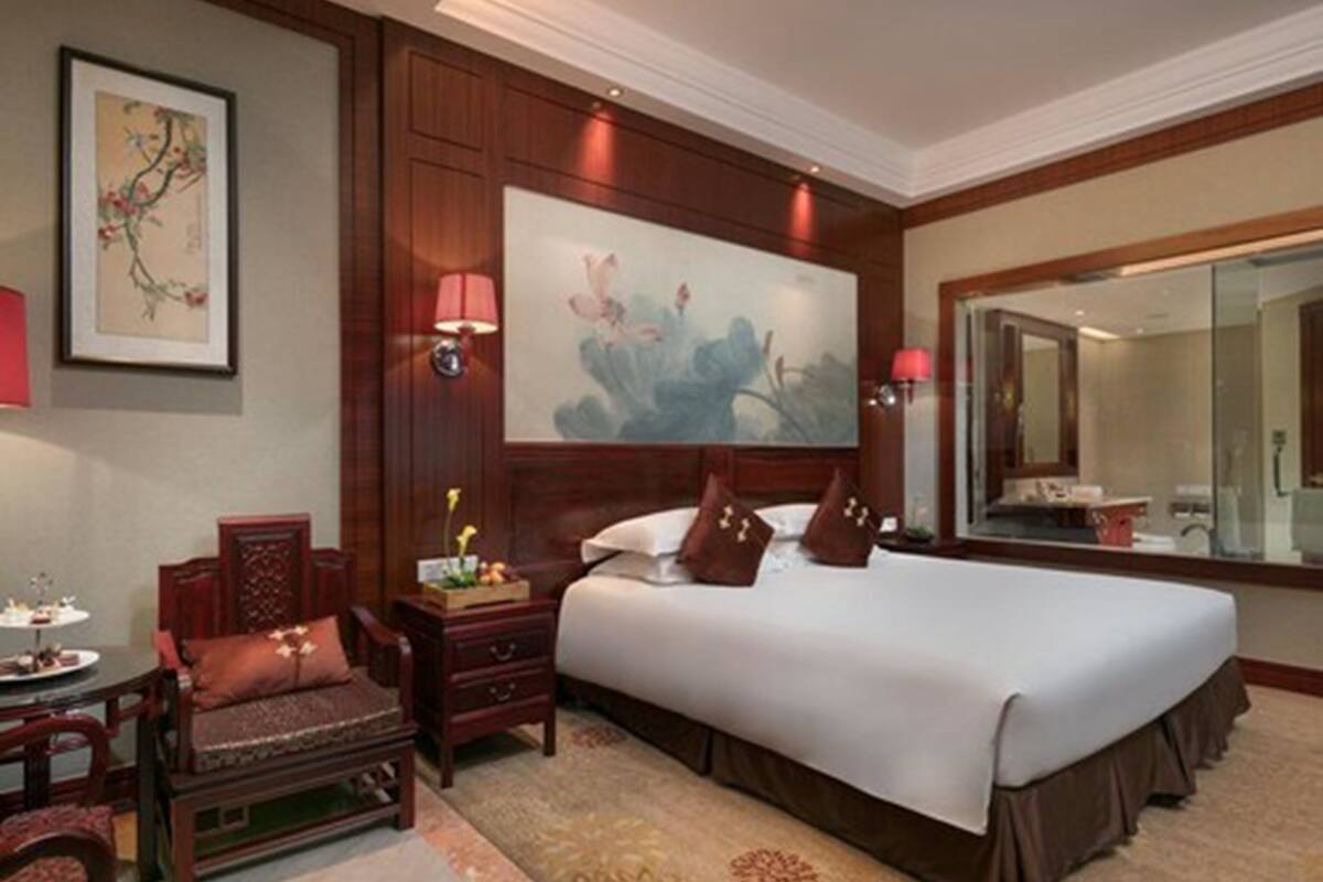 Une chambre d’hôtel avec un grand lit, une table de chevet en bois, une chaise, une petite table avec une lampe et un tableau au mur.