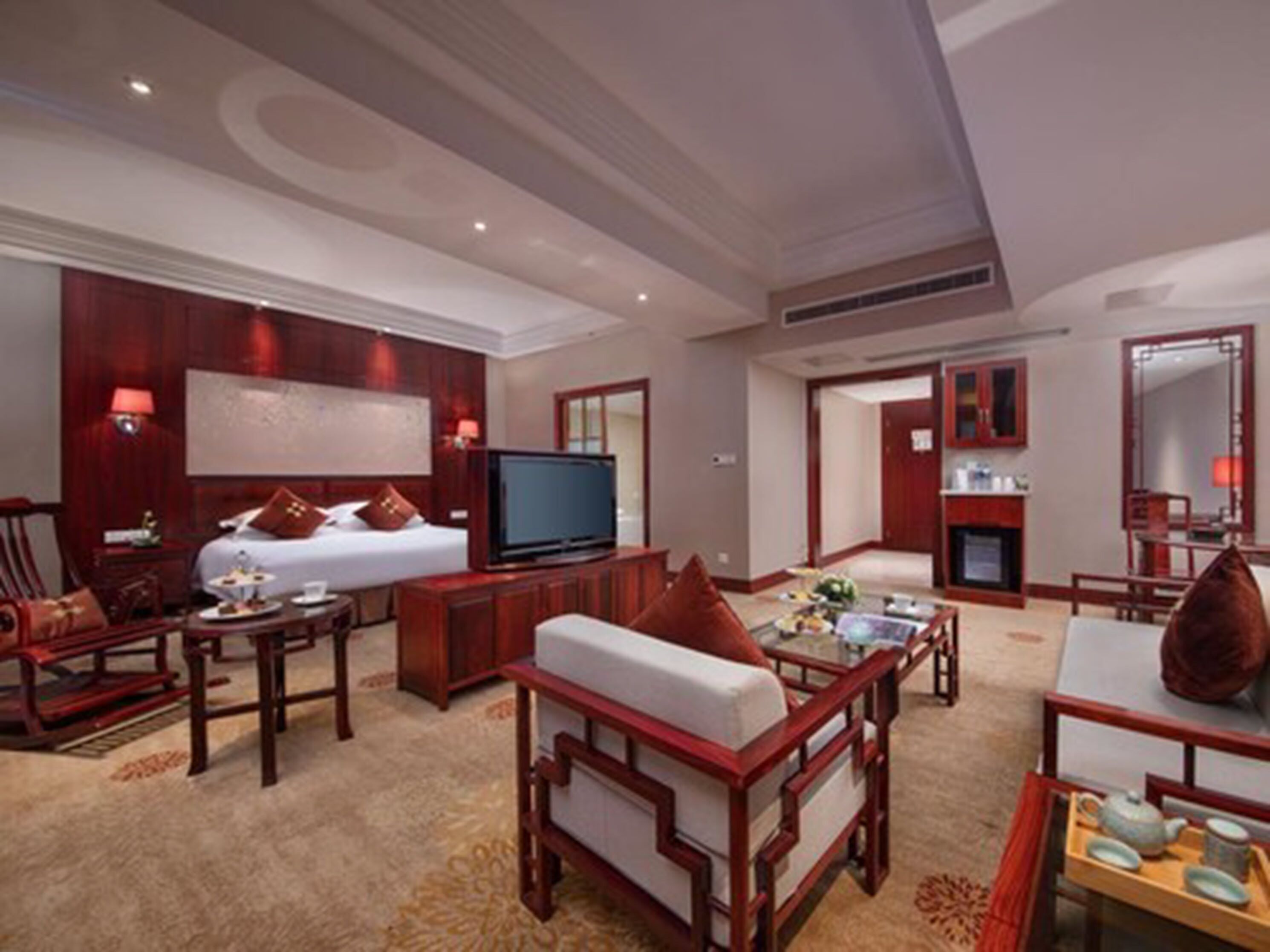 A hotel room with a bed, television, seating area with a sofa and chairs, a dining table with a tray of items, and a fireplace.