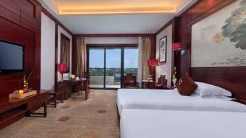 Habitación de hotel con una cama grande, un escritorio con silla, televisión y vistas al exterior.