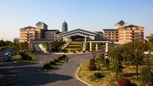 Um hotel grande com vários andares, entrada central com degraus e área de estacionamento.