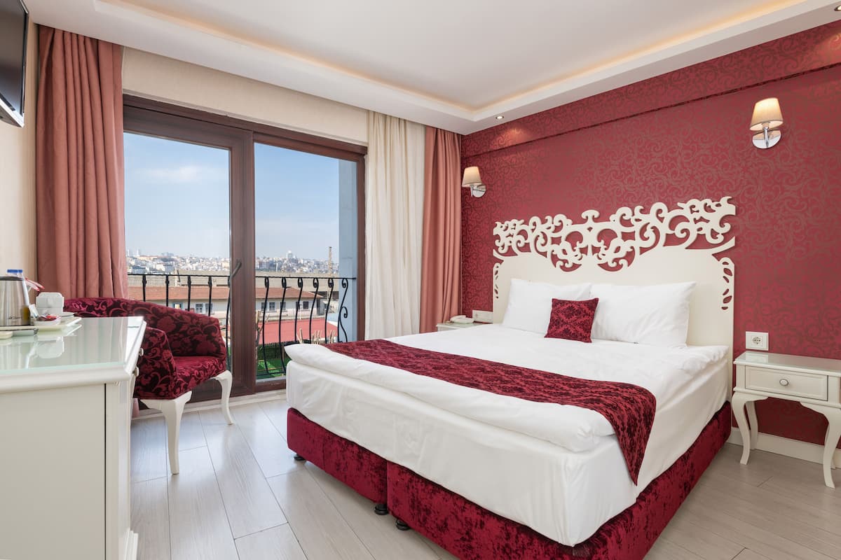 A hotel room with a large bed, a desk, and a view of the city through a balcony.