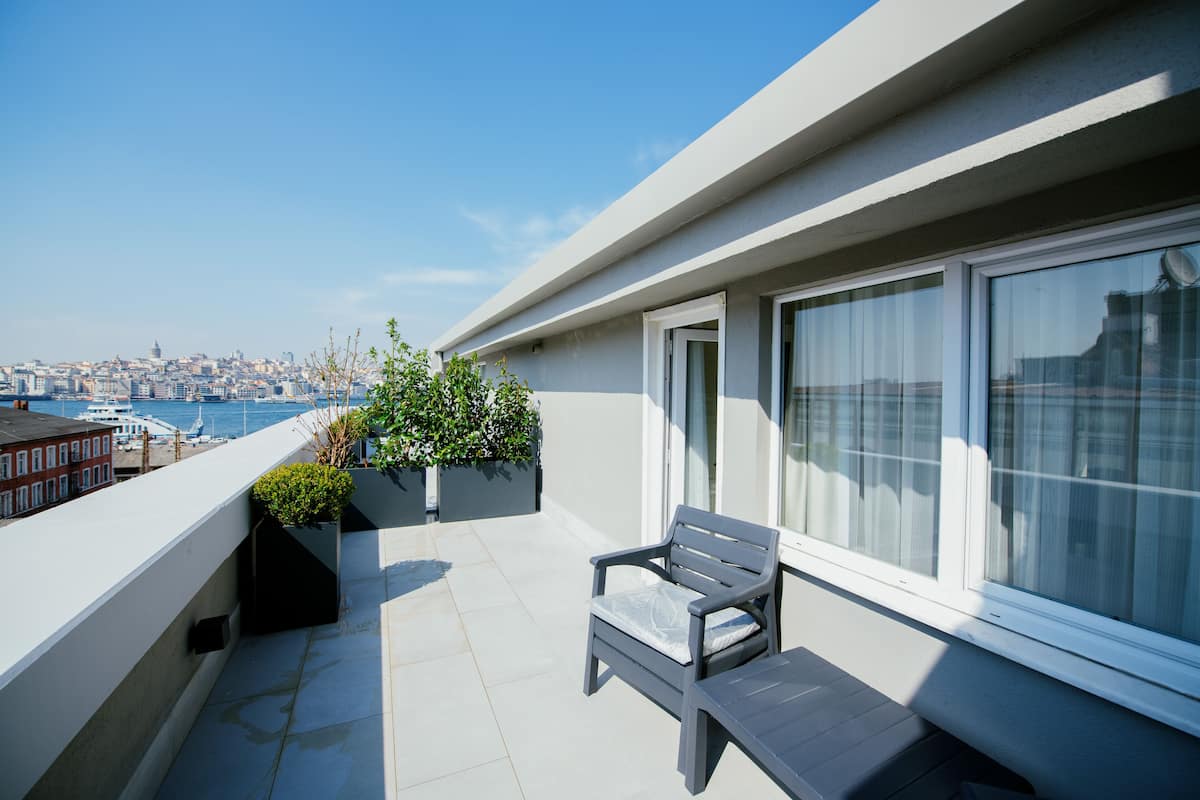 A balcony with a view of a cityscape and harbor, featuring a bench and potted plants.