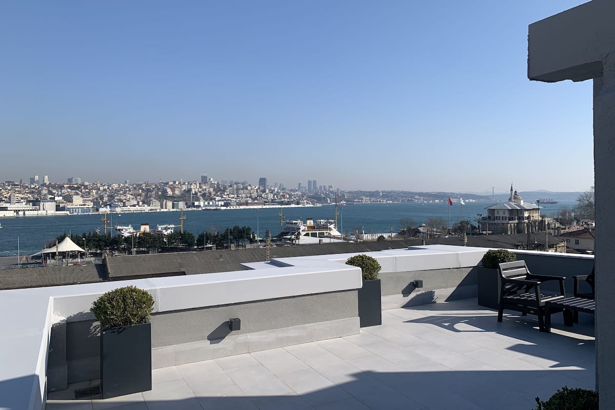 A rooftop terrace with a view of a city skyline and a body of water.