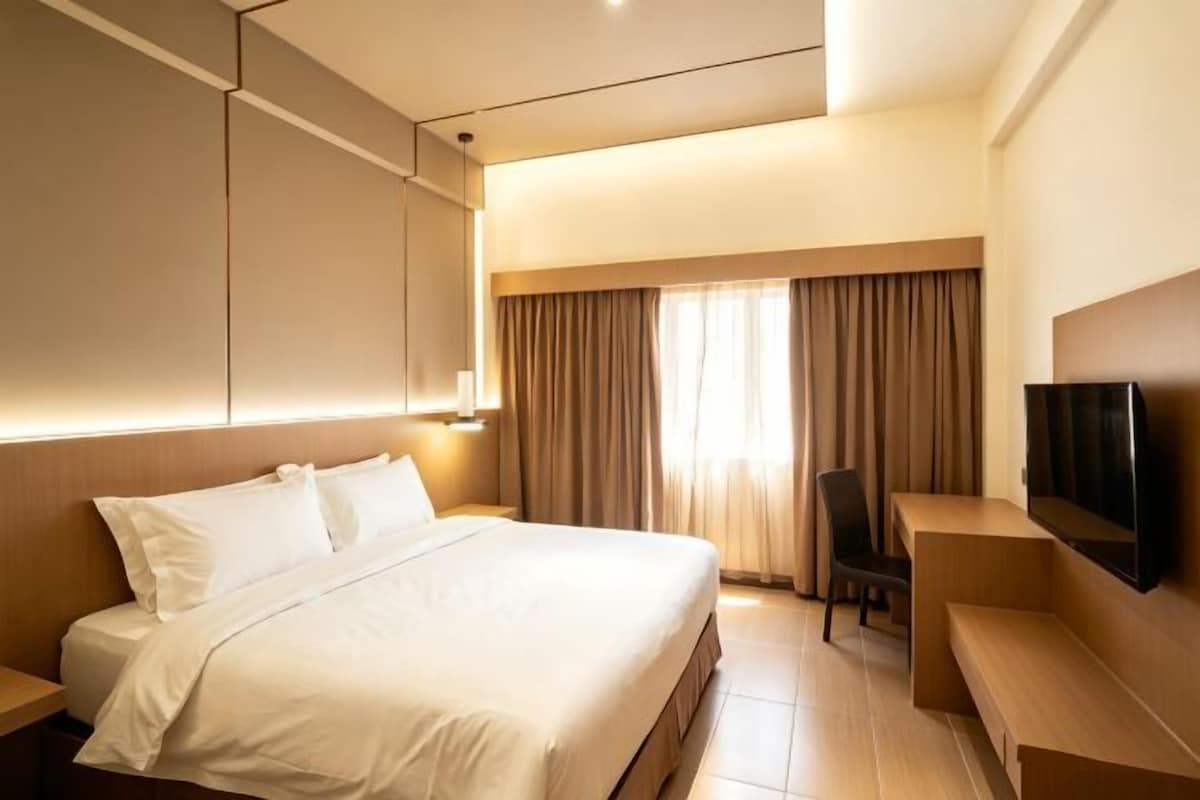 Une chambre d’hôtel avec un lit, un bureau, une chaise, une télévision et une fenêtre avec des rideaux.