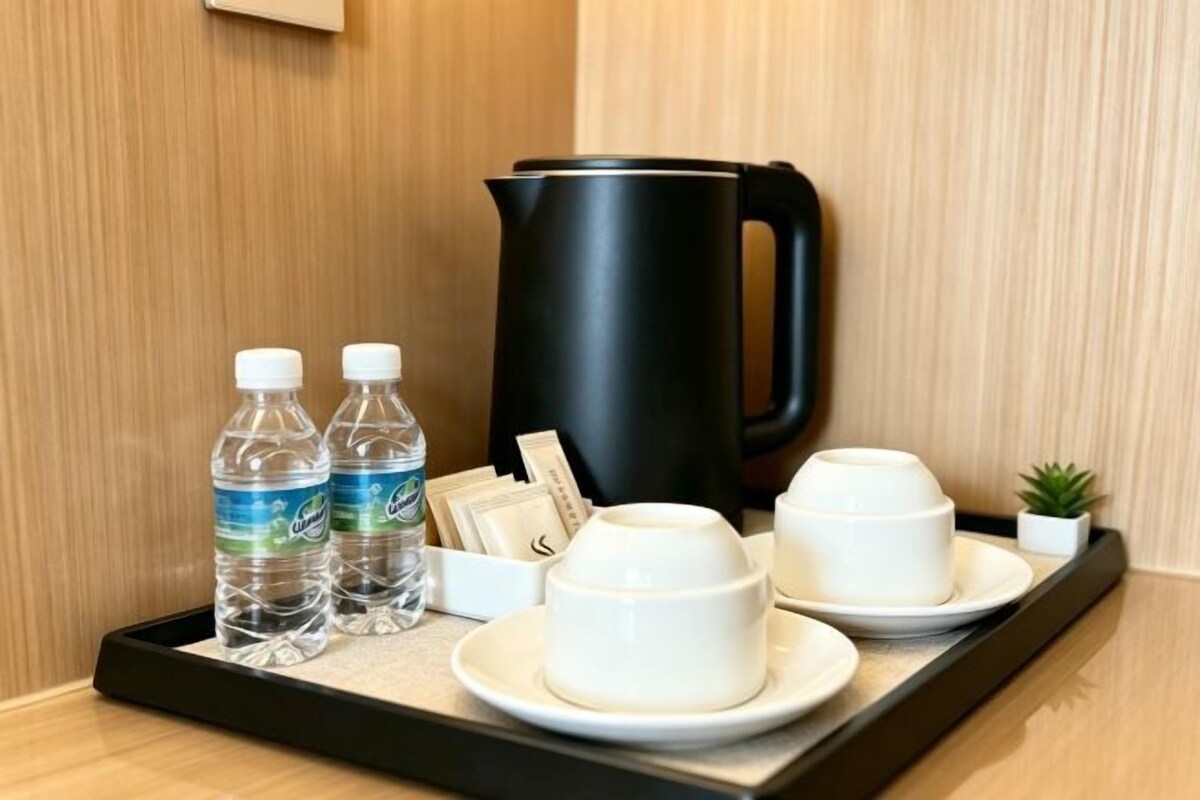 A tray with a black coffee pot, two water bottles, a small plant, and white cups and saucers.