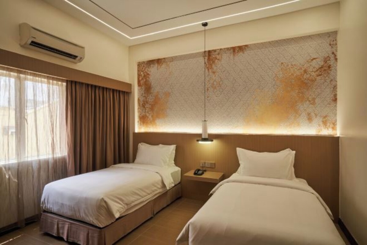 A hotel room with two beds, a nightstand, a wall-mounted air conditioner, and a large abstract painting.