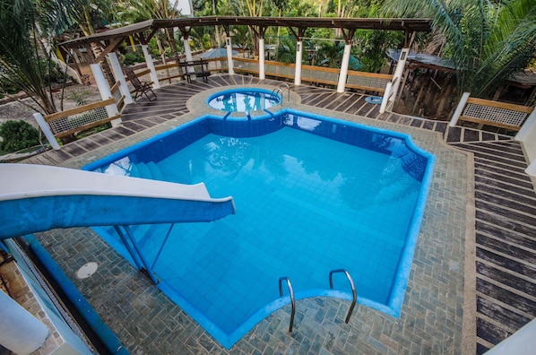 A rectangular swimming pool with a small circular hot tub, surrounded by a wooden deck and a covered seating area.