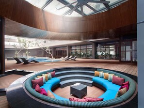 A modern indoor pool area with a circular seating area, lounge chairs, and a glass ceiling. - ibis Styles Jakarta Airport (Tangerang)