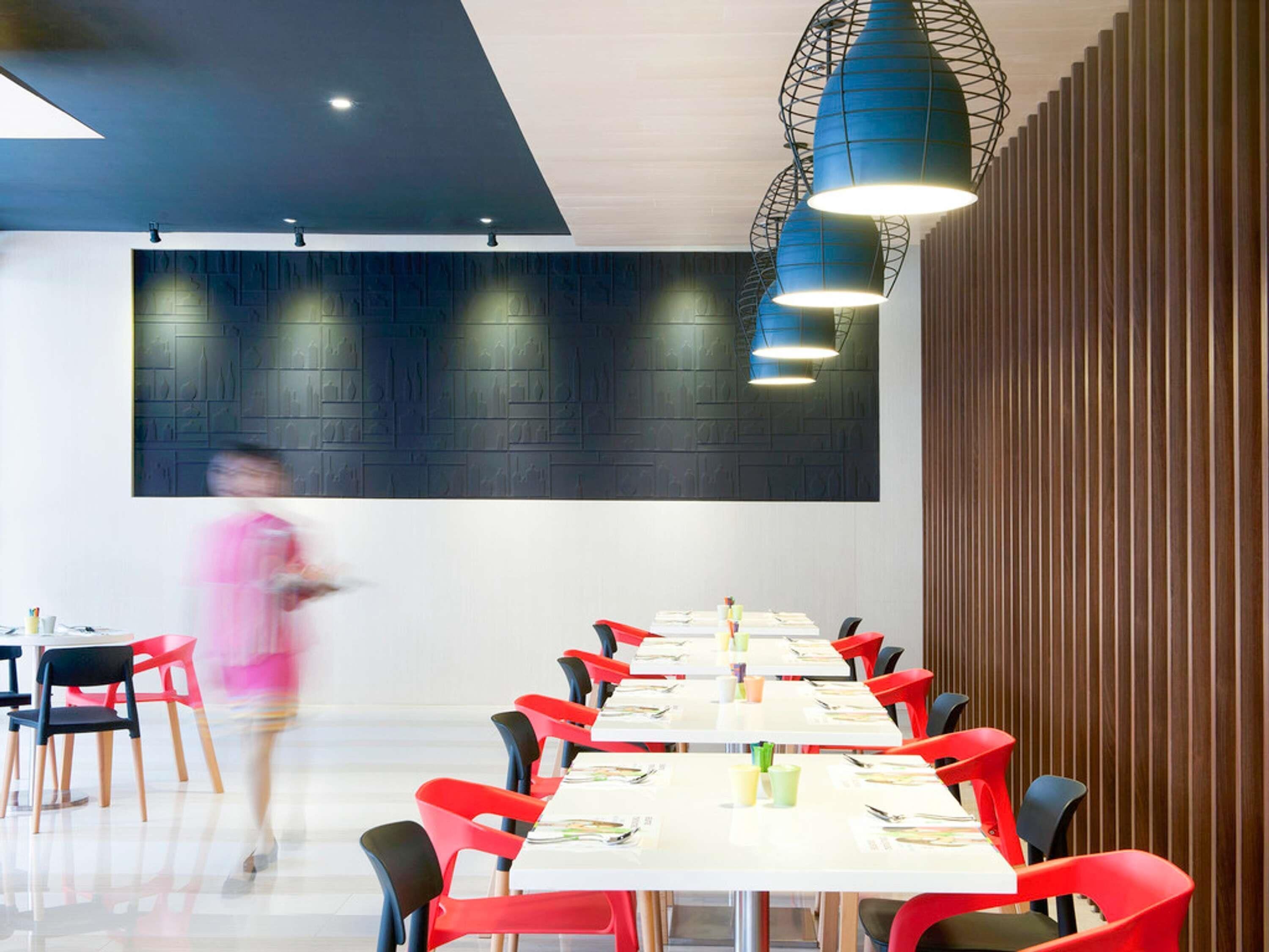 Un comedor moderno con una mesa larga, sillas rojas y lámparas colgantes azules.