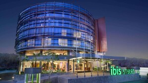 A modern hotel with a curved glass facade, a prominent entrance, and a sign reading "ibis styles". - ibis Styles Jakarta Airport (Tangerang)