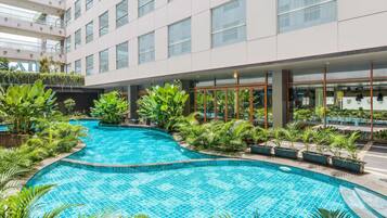 Un hotel moderno con una amplia piscina interior rodeada de exuberante vegetación y un edificio de varios pisos con grandes ventanales.