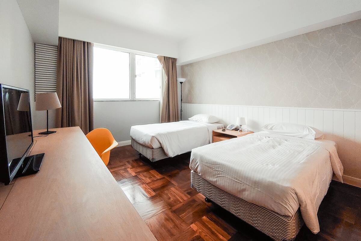 Habitación de hotel con dos camas, un escritorio, una silla, un televisor y una ventana con cortinas.