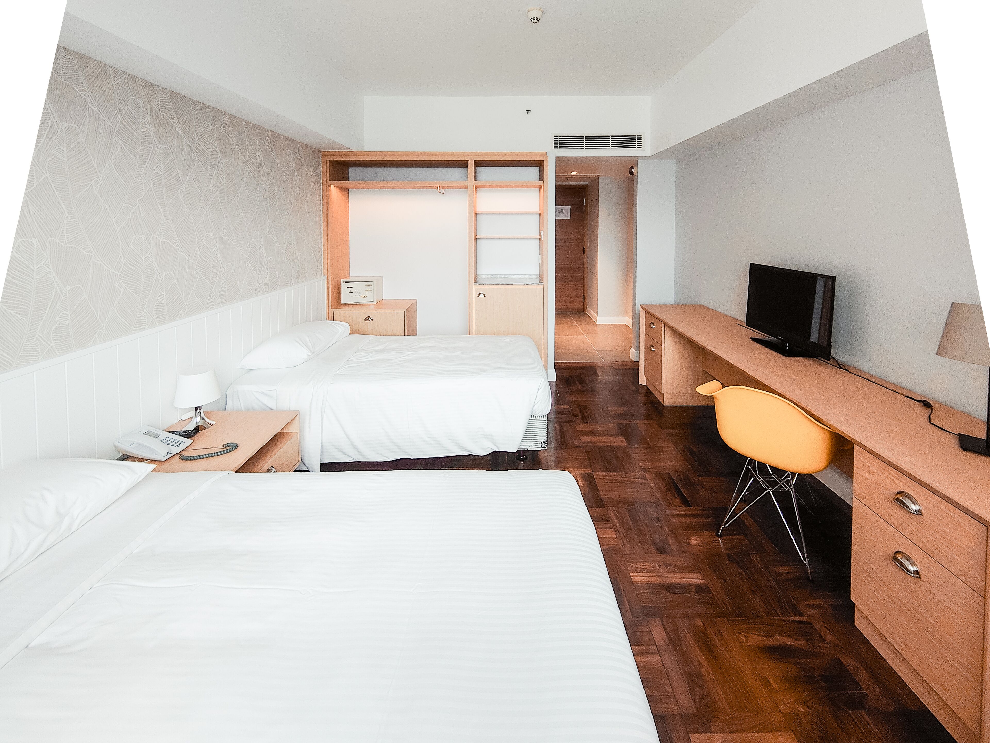 A hotel room with two beds, a desk, a chair, a television, and a wardrobe.