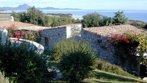 Un edificio de piedra con techo de tejas, rodeado de vegetación y vistas al mar.