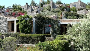Un edificio de piedra con una bandera, rodeado de abundante vegetación y flores rojas.