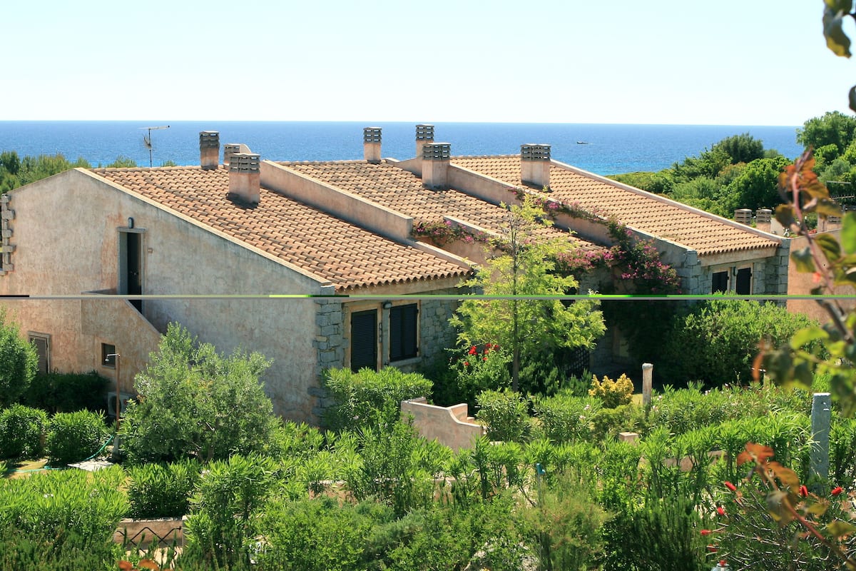 Un bâtiment situé sur la côte, doté d’un toit en tuiles, de murs en pierre et d’un jardin où poussent différentes espèces de plantes.
