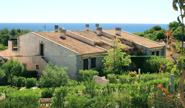 A coastal building with a tiled roof, stone walls, and a garden with various plants. - Le Residenze di Sant'Elmo (Castiadas)