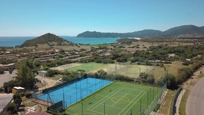 Vista aérea de una zona costera con una amplia piscina azul, canchas de tenis y edificios residenciales.